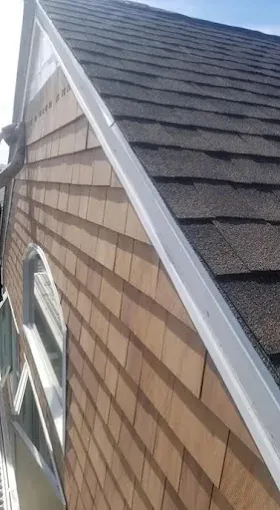 Close view of a newly fitted white gutter along a shingled roof edge