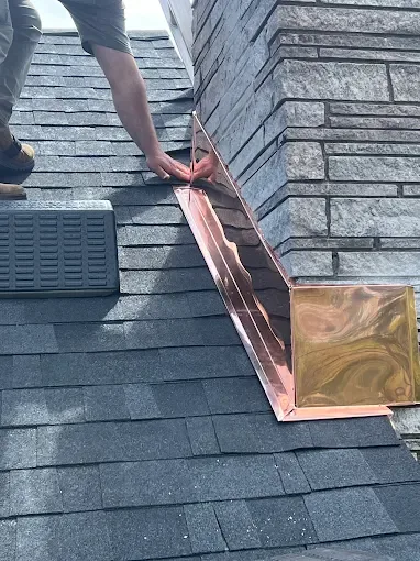 Roofer fitting new copper step flashing against a stone chimney